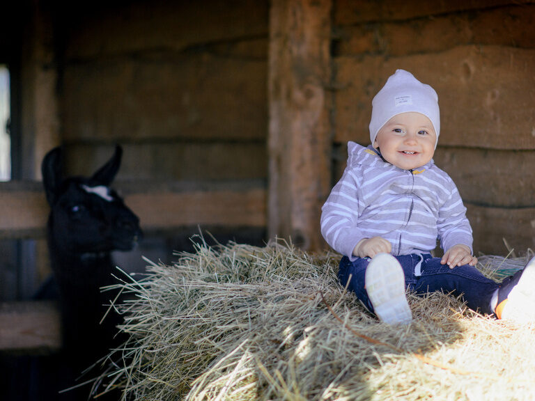 Ein Kleinkind sitzt lächelnd auf Stroh beim Tonihof.