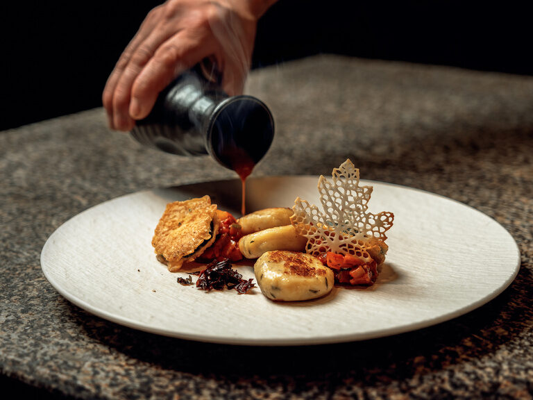Ein Koch veredelt im Musikhotel Tonihof im Bayerischen Wald kunstvoll angerichtete Speisen mit einer delikaten Sauce.