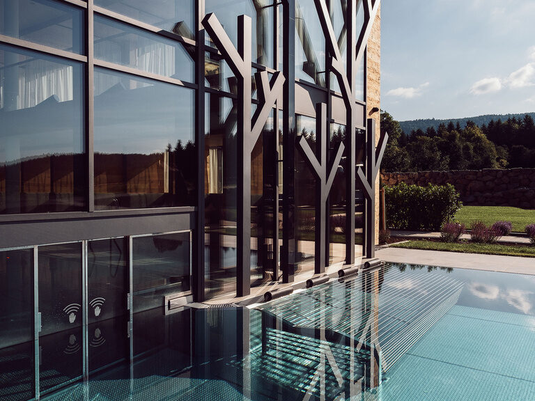Im Licht der untergehenden Sonne spiegelt sich der Außenpool des Tonihofs mit blick auf das imposante Hotelgebäude.