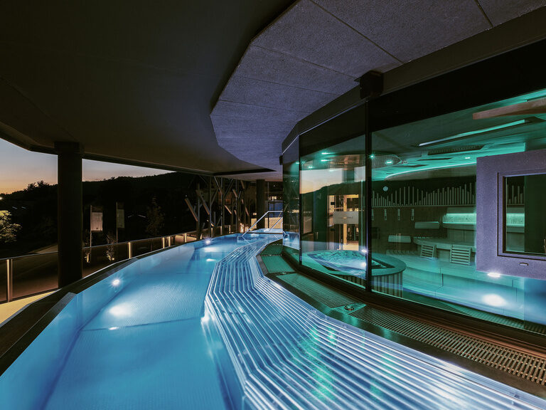 Der blau beleuchtete FKK Skypool vor der eindrucksvollen Architektur des Hotels Tonihof.