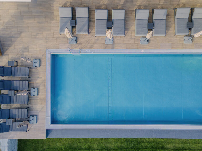 Luftaufnahme des großen Pools des Wellnesshotels Tonihof mit mehreren gemütlichen Sonnenliegen.
